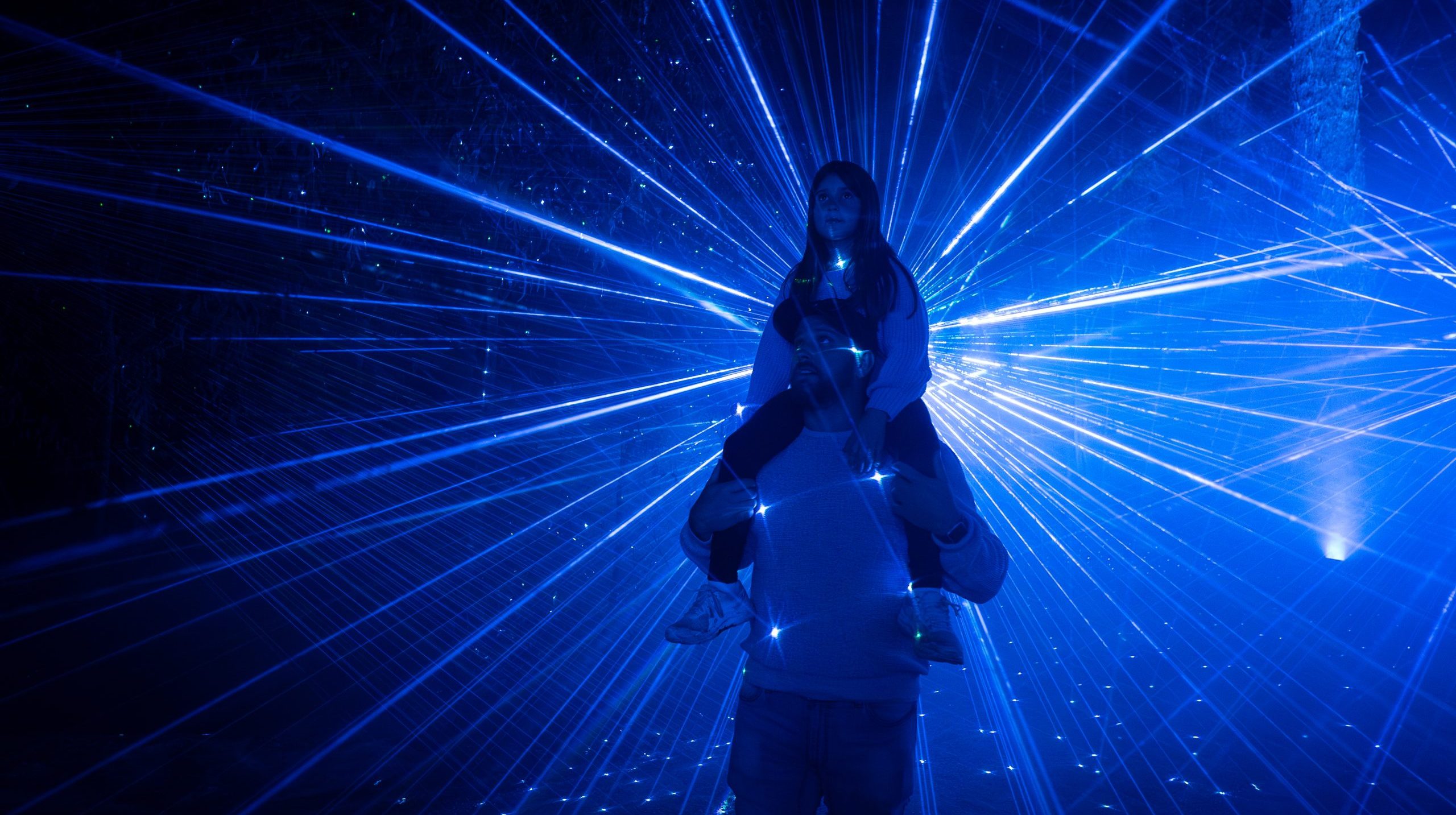A girl sits on her dad's shoulders as they explore a blue lit laser section during Bullanginya Dreaming.